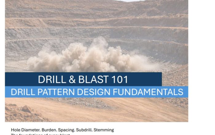 A blast firing on an open pit bench, throwing dust across the pit